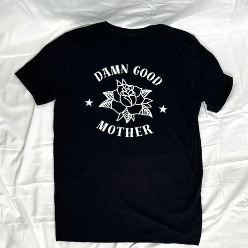 A black short-sleeve t-shirt laid flat, featuring a white graphic print on the back with a rose, stars, and the text 'DAMN GOOD MOTHER'.