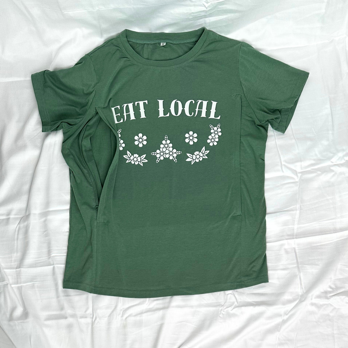 A green short-sleeve t-shirt with 'EAT LOCAL' and a floral pattern printed in white, nursing side zip access highlighted.