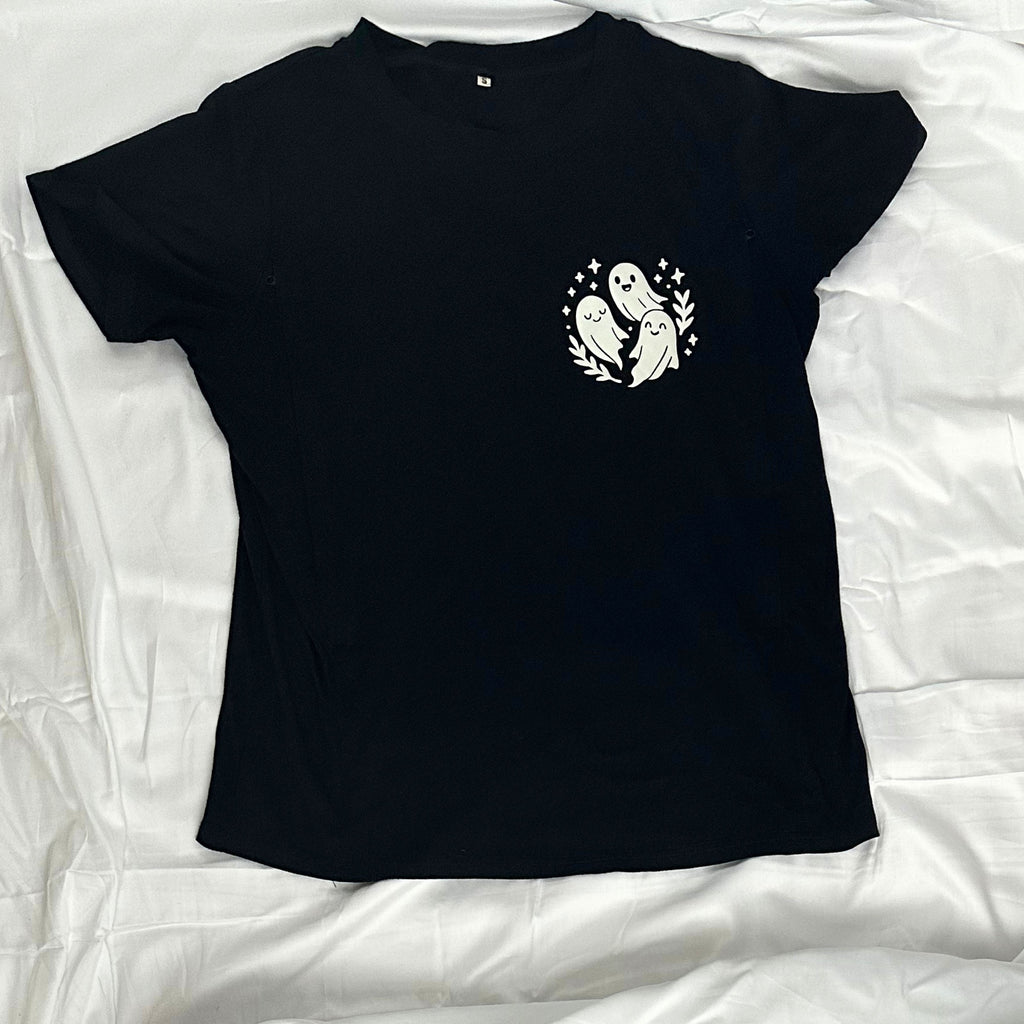 A black short-sleeve t-shirt laid flat, featuring a small white graphic on the left chest of three ghosts inside a circular wreath with stars.